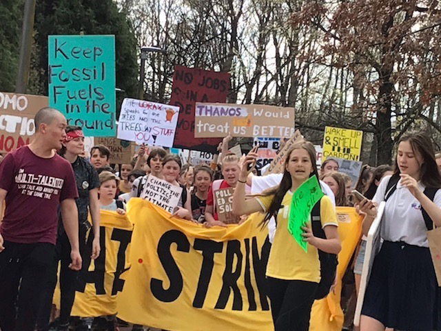 School students carry banners and signs through a city park.